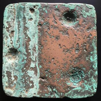 Close up view of a weathered square metal object with green patina and rough textured surface showing signs of age and corrosion photo