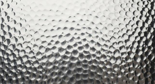 Close up textured surface of frosted glass with a hammered or dimpled pattern creating diffused light and shadow effects photo