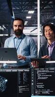 Vertical Portrait of smiling engineers in data center code with assistance. Happy IT experts doing brainstorming, leveraging artificial intelligence large language model to solve tasks, camera A video