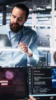Vertical Data center manager coordinating programmers fixing critical error while using AI. Server room team leader overseeing workers repairing glitch popup while using artificial intelligence, camera A video