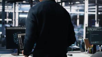 Admin entering data center office, reviews AI diagnostics on computer. IT expert starting work at server farm desk, optimizing artificial intelligence systems configuration, camera A video