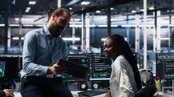 gerente supervisando mujer en datos centrar codificación con asistencia. supervisor supervisa trabajo por africano americano eso experto apalancamiento artificial inteligencia grande idioma modelo, cámara un video