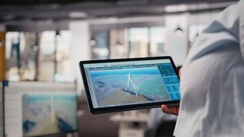 stänga upp av tekniker använder sig av läsplatta till arbete på trogen vind turbin designad för rena energi produktion. arbetstagare svep på pekskärm enhet, design skärande kant vawt innovation, kamera en video