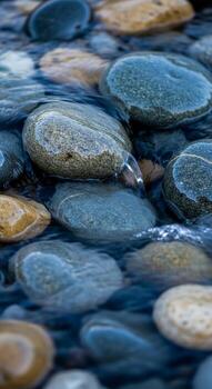 Smooth rounded river stones submerged in clear shallow water creating a serene and natural abstract pattern of blues and earth tones photo