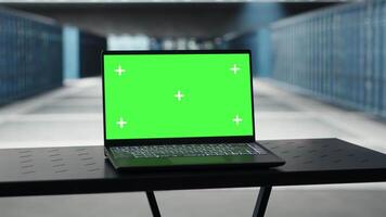 Green screen laptop in high tech data center facility with multiple rows of fully operational server racks. Mockup notebook used to oversee server hub built for digital storage systems video