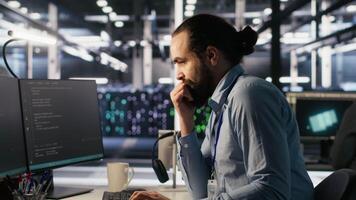 Engineer in data center frustrated by critical error popup on monitor during diagnostics session. IT expert stressed while troubleshooting system fault affecting infrastructure performance, camera A video