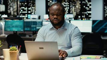 africano americano analista meditando di possibile risultati per un' problema a stazione di lavoro dopo ore, intenso concentrazione per valutare proiezioni con logico deduzione e osservazione. telecamera b. video