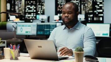 ritratto di maschio lavoratore immersa nel lettura messaggi di posta elettronica e ricercando dati per un' multinazionale azienda, Lavorando dopo ore nel un' buio ufficio. messa a fuoco su obiettivi per sviluppo. telecamera b. video