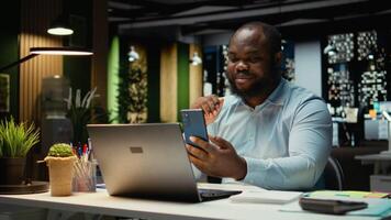 Black employee chatting late at night on phone web teleconference, engaged in a digital discussion for productivity. Interacting with shareholders. Networking session in corporation. Camera A. video
