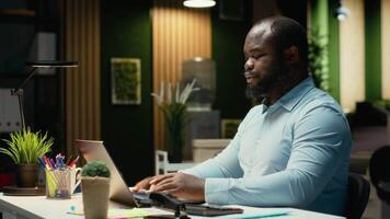 ritratto di nero maschio analista sorridente e Lavorando in ritardo dopo ore, rivedere dati intuizioni per incontrare attività commerciale obiettivi, soluzione budgeting compiti a notte e fatto controllo documenti. telecamera b. video