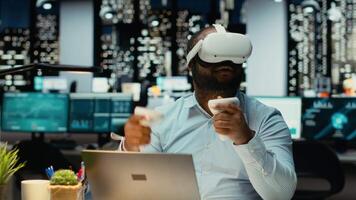 Black male worker using VR glasses and gadgets to draft a project plan, forecasting projections and documenting risk assessment results. Organizing tasks for business goals. Camera B. video