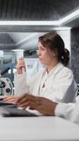 Vertical Scientist records observations from laboratory experiment for research documentation and validation of clinical results. Woman doing data logging, taking notes, confirming lab findings, camera A video