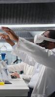 Vertical Scientist using computer and VR headset equipment for DNA data analysis in laboratory. African american man using bioinformatics genomics software and virtual reality tech in modern lab, camera A video