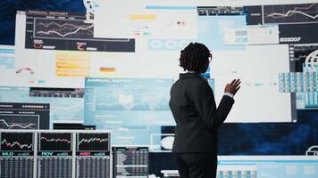 Business manager showing graphs on digital screens at event, telling audience how to increase company profits. Woman speaking in mic at conference, showing KPI metrics on digital screen, camera A video