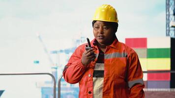 porträtt av leende borrning rigg expert- talande i walkie talkie, håller på med snabbt svar samordning. glad kvinna på offshore plattform lyssnar till instruktioner genom handhållen radio, kamera b video