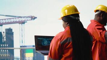 Engineer on offshore platform deck using artificial intelligence software on laptop to optimize drilling operations. Teamworking colleagues monitoring barge activity using AI technology, camera B video