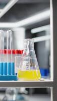 Vertical Close up of colorful chemical solutions inside scientific glassware on lab shelf. Reagents in vials ready to be used for experimental analysis inside empty high tech research center, panning shot video