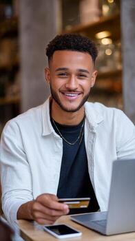 Smiling Young Man at a Cafe Using Laptop and Holding a Credit Card for Online Shopping photo