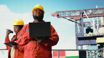 Mann Arbeiten zum industriell Off-Shore Plattform Überwachung Operationen auf Deck mit Laptop. afrikanisch amerikanisch Bohren rig Mitarbeiter Überprüfung Energie Operationen mit Notizbuch, Kamera b video