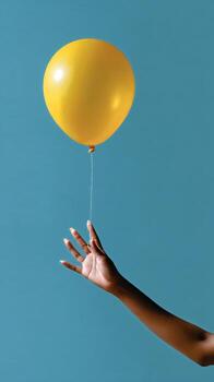 Person Holding a Yellow Balloon Against a Blue Background in a Playful Display of Joy photo