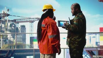 soldat sur offshore Plate-forme plate-forme parlant avec technicien, en utilisant dispositif visualisation logiciel. africain américain naval unité gardes forage plate-forme contre terroriste des menaces en utilisant tablette application, caméra une video
