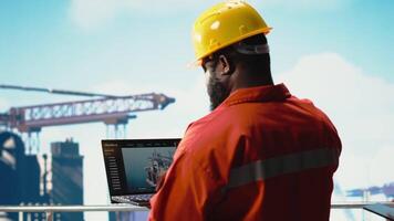 Fossil Treibstoff Unternehmen Experte mit Laptop Software zu bestimmen optimal Bohren rig Standorte. afrikanisch amerikanisch Mann auf Off-Shore Plattform suchen beim Gut Websites Daten auf Notizbuch, Kamera b video