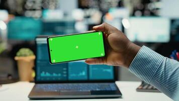 African american guy looks at mockup display on phone at night, solving business tasks after hours. Office consultant working on project development, meeting targets and goals. Camera B. video