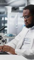 vertikal labb specialist håller på med genetik studie använder sig av klinisk Utrustning, avlägsnande glasögon, kontroll analys resultat på dator. man använder sig av vetenskaplig redskap på arbetsbänk, håller på med komplex experiment, kamera b video