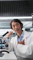 Vertical Team of multiethnic microbiologists working together in lab with molecular microscope. Multiracial colleagues in research facility using optical device gear to examine medical tissue, camera A video