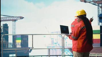 Engineer on offshore platform deck using artificial intelligence software on laptop to optimize drilling operations. Teamworking colleagues monitoring barge activity using AI technology, camera A video