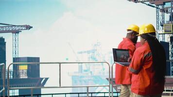 Off-Shore rig Arbeiter auf Öl Plattform Deck Überwachung Operationen mit Laptop Software Laptop. Bohren rig Experte Überprüfung Energie Operationen mit Notizbuch, Prognose Ausrüstung Versagen, Kamera ein video