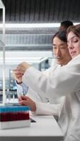 vertical mayor laboratorio experto y aprendiz analizando lote de sangre muestras para enfermedad investigación clínico pruebas. laboratorio gerente y interno haciendo investigación en optimista fluido viales para pruebas, cámara un video