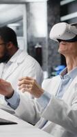 verticale laboratorio specialista indossare vr cuffia attrezzatura utilizzando chimico fluidi per esperimenti. chimico usi virtuale la realtà dispositivo per simulare utilizzando soluzione laboratorio cristalleria a postazione di lavoro, telecamera B video