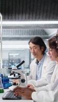 Vertical Senior researcher records observations from coworkers using microscope to evaluate cellular structures. Man taking notes of medical tissue observation through magnification tool, camera A video