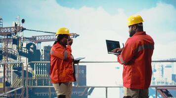 offshore plattform besättning använder sig av artificiell intelligens program på bärbar dator till optimera borrning operationer. afrikansk amerikan medarbetare analyserar geologi data använder sig av ai tech på anteckningsbok, kamera en video