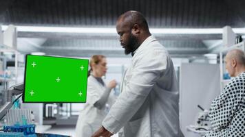 Green screen next to black medic studying data for drug testing in lab, evaluating dosage and potential side effects. Checking chemical reactions and safety to support science breakthrough. Camera B. video