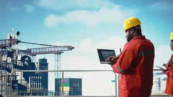 Fossil Treibstoff Unternehmen Experte mit Laptop Software zu bestimmen optimal Bohren rig Standorte. afrikanisch amerikanisch Mann auf Off-Shore Plattform suchen beim Gut Websites Daten auf Notizbuch, Kamera ein video