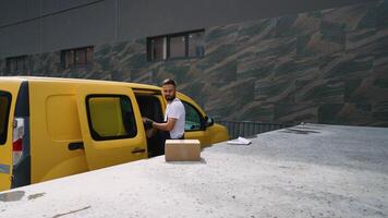 Delivery man unloading cardboard boxes from van at warehouse loading dock video