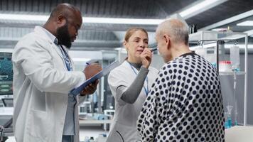 verschillend wetenschappers het uitvoeren van observatie en examen van een geduldig in een Onderzoek laboratorium, testen een nieuw behandeling en analyseren dosering Effecten. aan het studeren risico's en resultaten voor voortgang. camera b. video