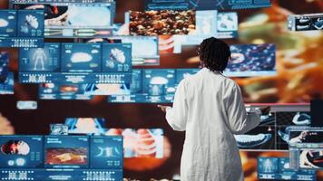 sorridente cuidados de saúde investigador hipnotizado de futurista médico dados visualizações, trabalhando em doença prevenção pesquisar. cientista admirados de Alto tecnologia paciente scans em digital interface, Câmera uma video