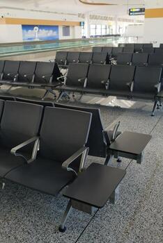 Empty airport waiting area with modern black seats and tables, bright lighting, and a view of a swimming pool in the background photo