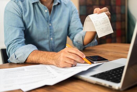 Male company manager holds transaction check adding source of additional income in tax form for correct filling of papers sitting at workplace with laptop in office photo
