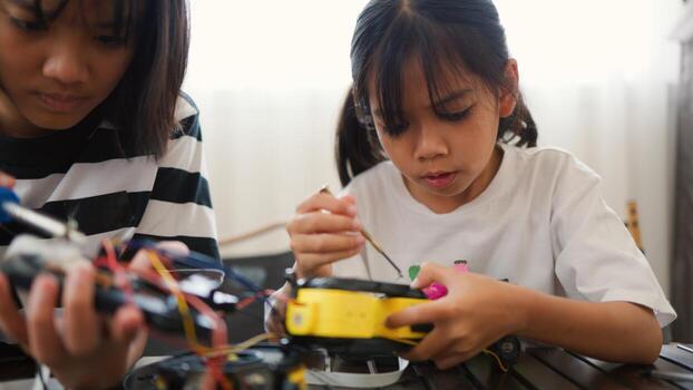 Two Asian girls working together on robotics project at home. Promoting STEM education, teamwork, coding, and problem-solving through hands on engineering and creative learning. photo