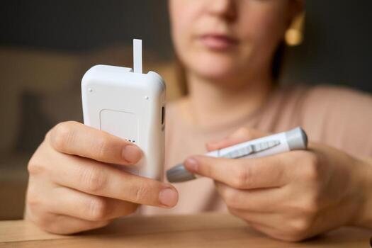 A user carefully handles a glucometer and a pen while checking blood sugar levels in a warm, inviting indoor atmosphere. The focus is on health management and daily routines photo