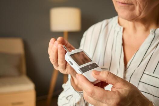A person is using a glucometer to check their blood sugar levels in a comfortable, well-lit room. A soft lamp and simple furniture create an inviting atmosphere photo
