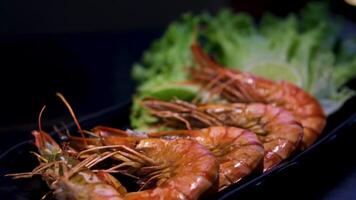 fyra kokta räkor kryddat med kryddor är anordnad på en vit tallrik med färsk sallad och tomat skivor, skapande en enkel och friska måltid alternativ. topp se, över huvudet video