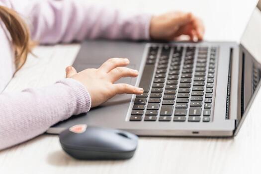Hands of a child sitting in front of a laptop while learning, chatting or playing photo