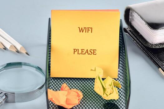 A bright yellow sticky note reads WIFI PLEASE, placed in a desk organizer with crumpled paper and writing tools. The neat workspace reflects a desire for internet connection photo
