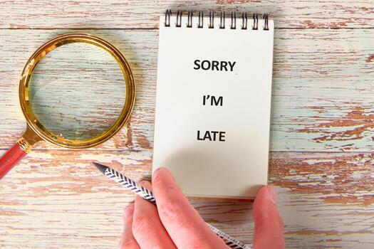 un mano sostiene un cuaderno abierto demostración el texto lo siento estoy tarde siguiente a un aumentador vaso y un estampado lápiz en un afligido de madera mesa foto