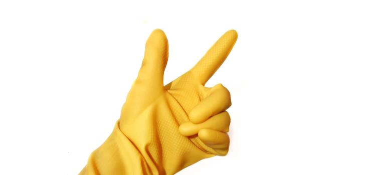 Hand in yellow rubber glove showing victory index finger sign isolated on white background photo
